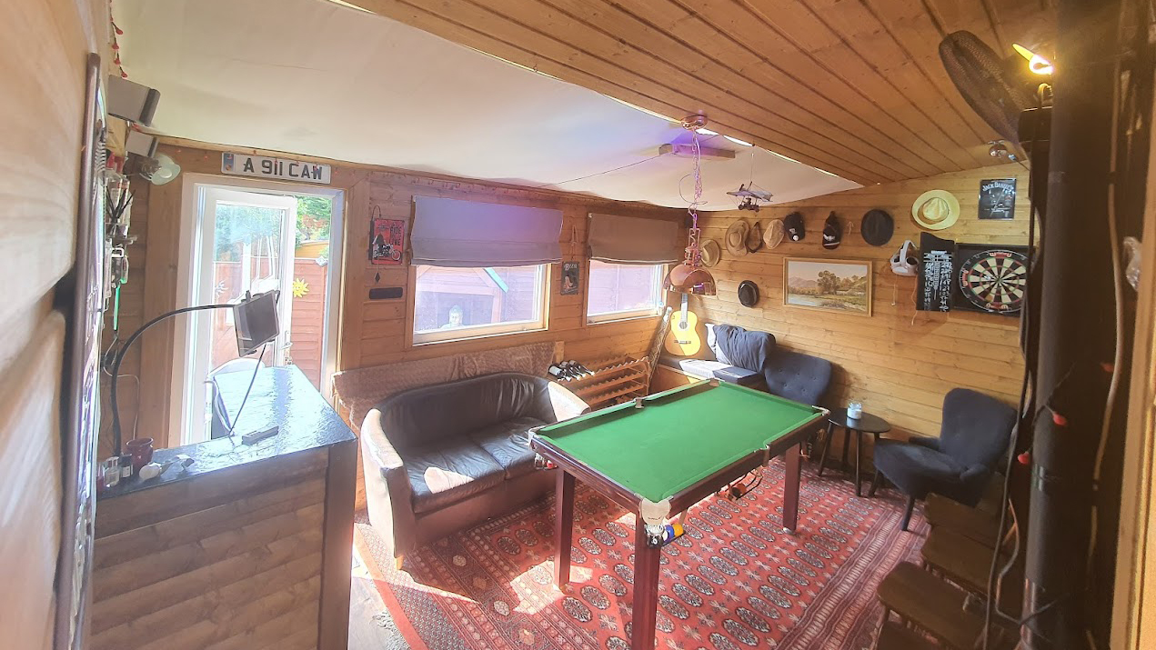 Wide camera angle of a mancave, with a pool table, bar, tv and seating area.