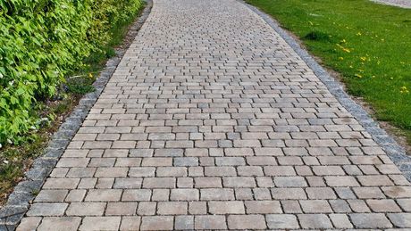 Grey pavement created in between grass with a hedge on the left.