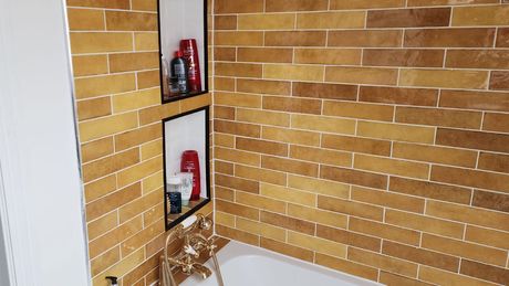 Image of brown tiles on a bathroom wall with shampoo and shower gel in a niche.